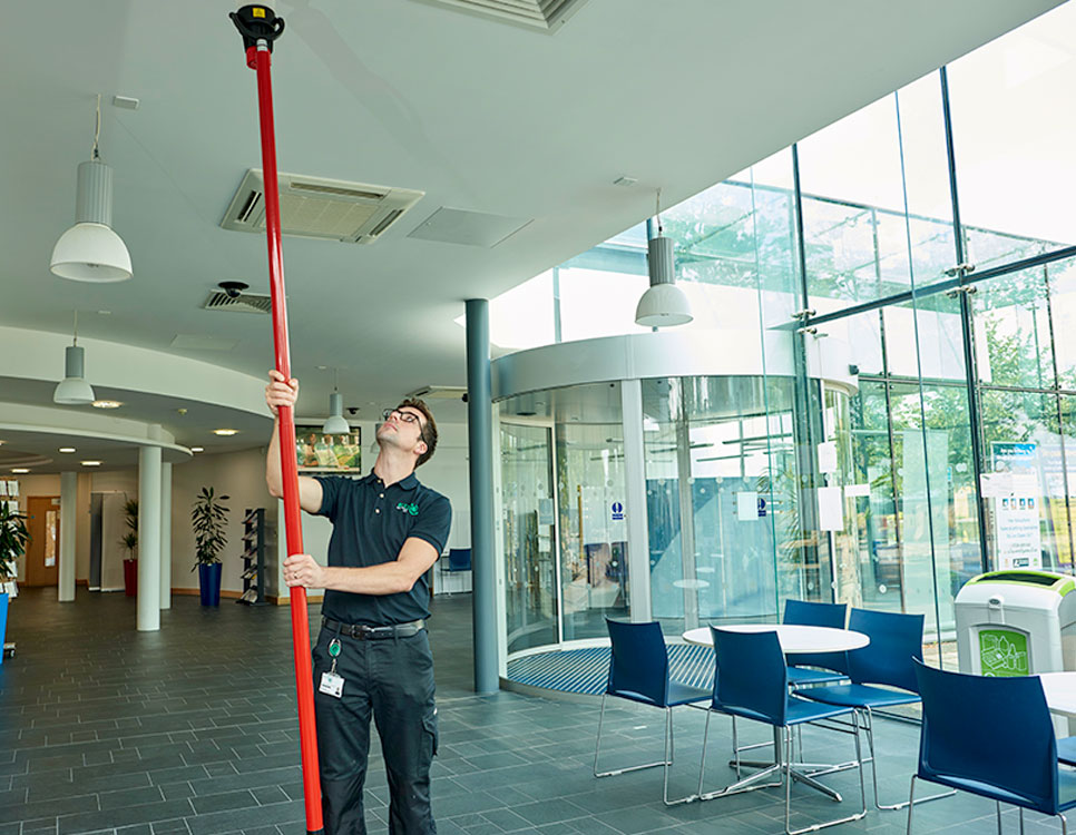 Electrician using long pole to reach fire alarm high up